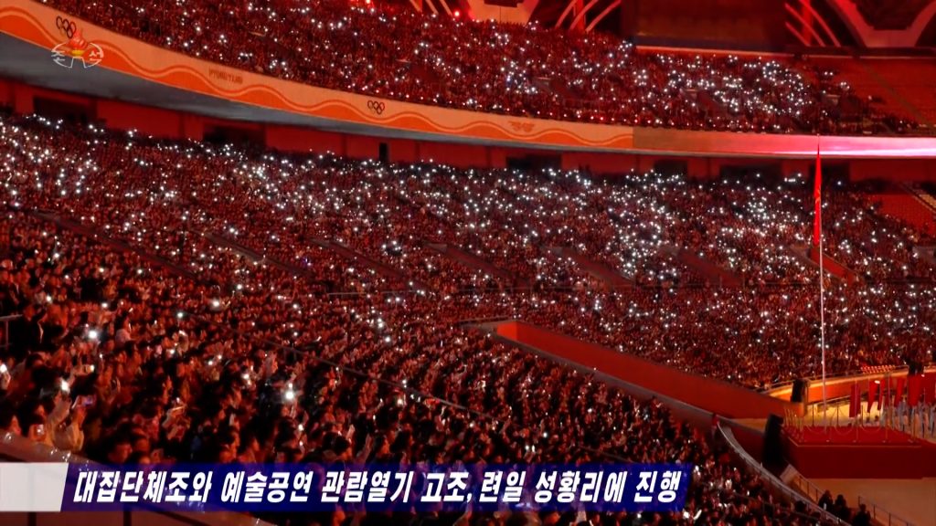 A large crowd of people in a stadium holding their smartphones to film an event, and use their smartphone flashlights