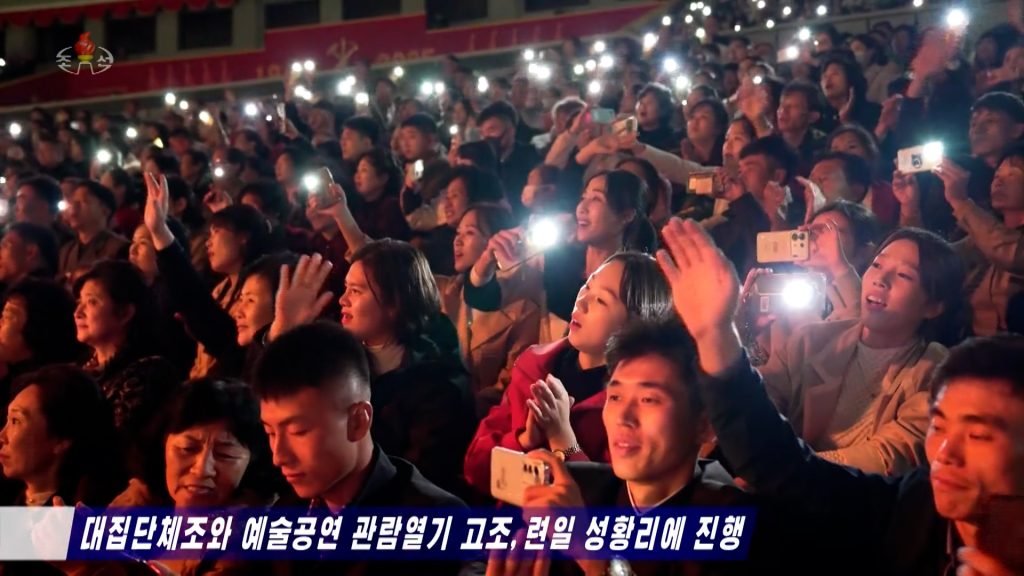 A large crowd of people in a stadium holding their smartphones to film an event, and use their smartphone flashlights